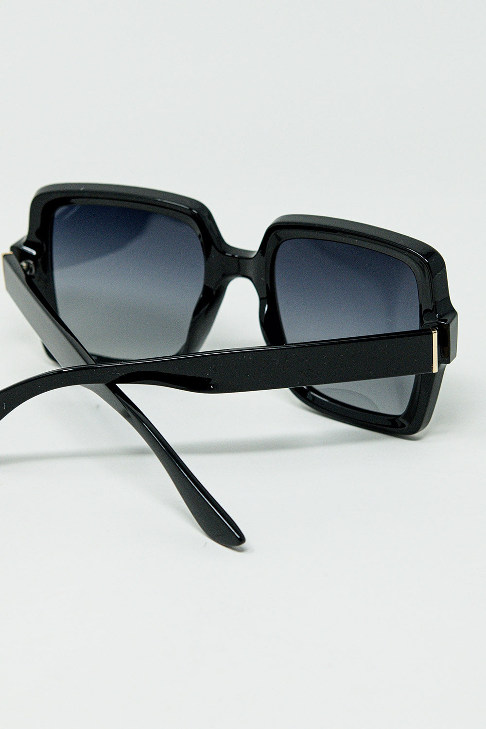 Gafas de sol de montura cuadrada ancha con detalle dorado en las patillas.