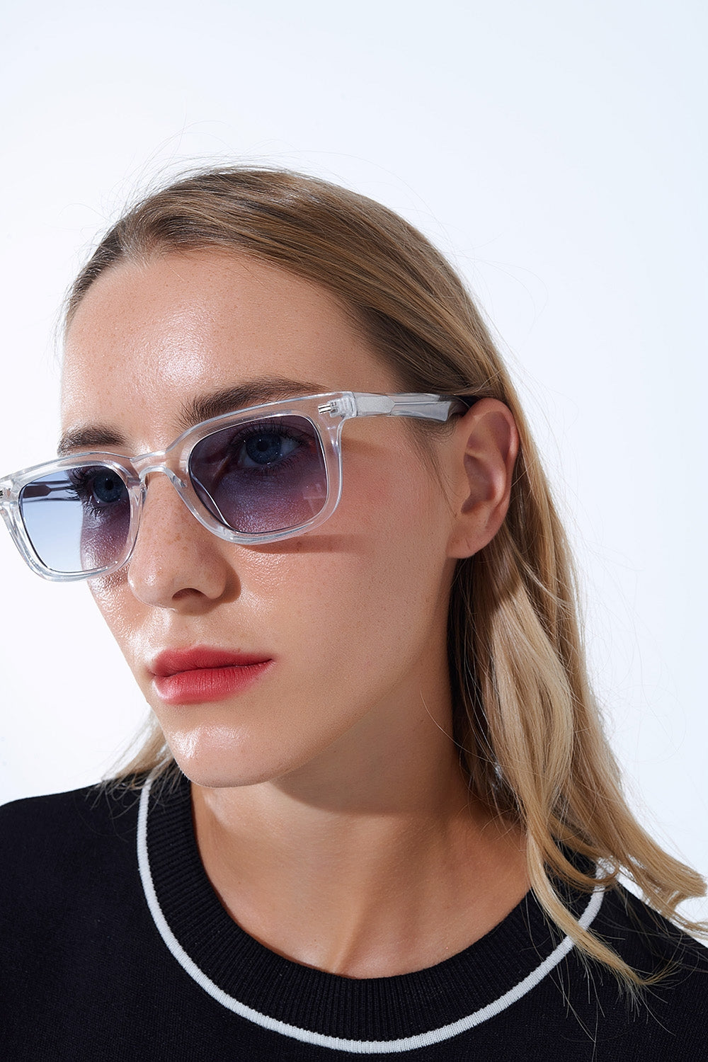 Mujer con gafas de sol cuadradas montura transparente y lentes azules degradadas.