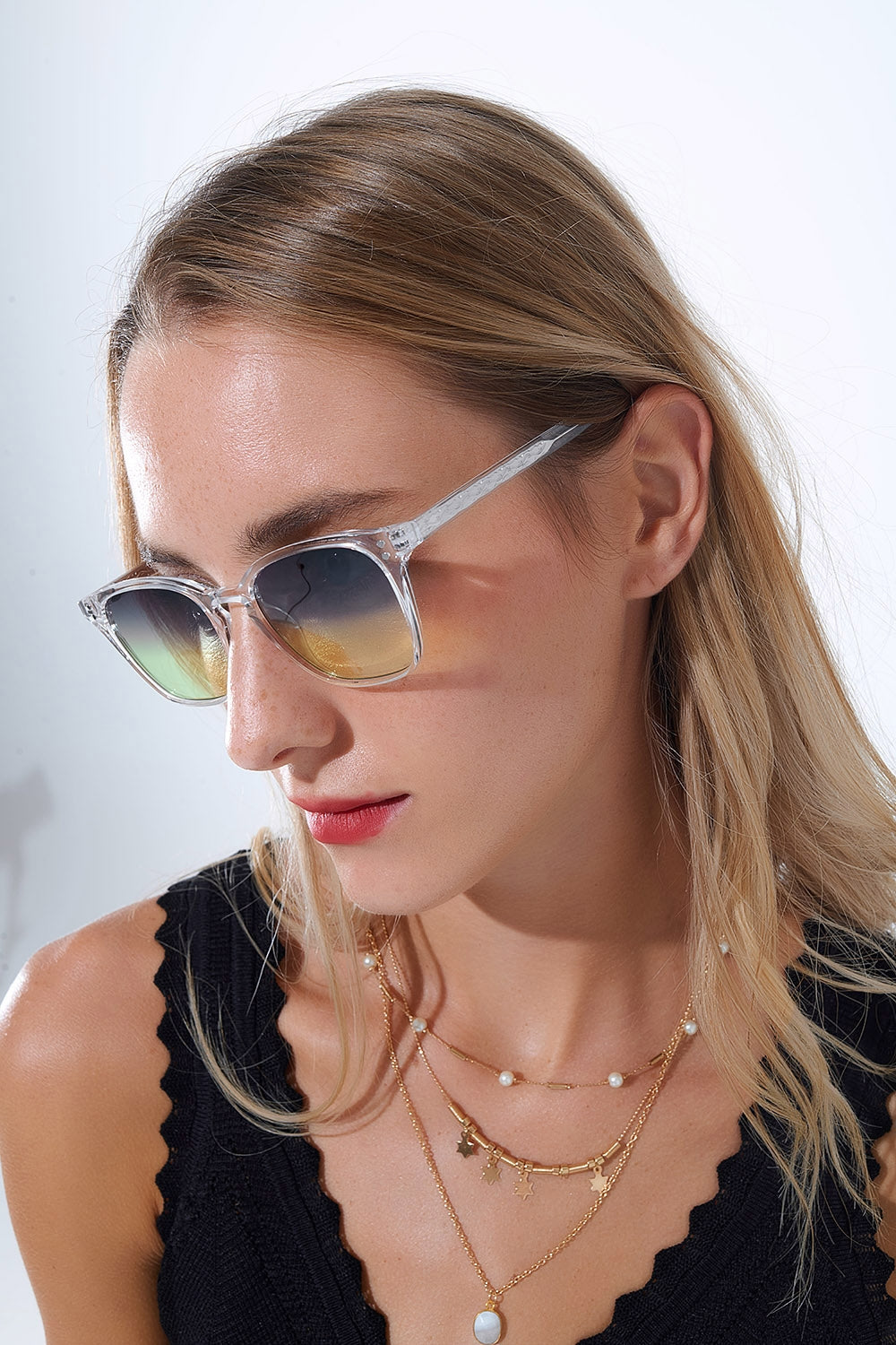 Mujer con gafas de sol cuadradas montura transparente y lentes verdes degradadas.