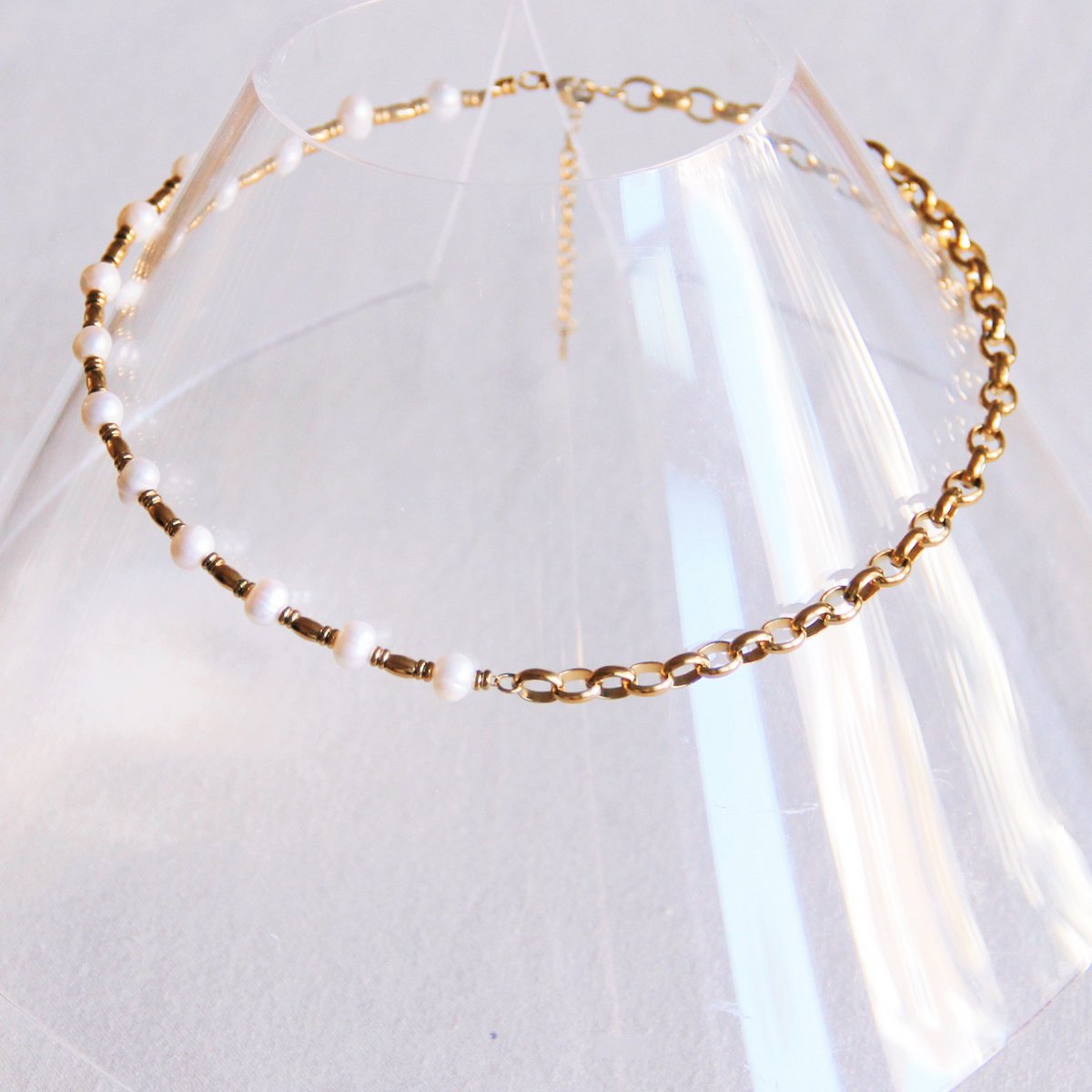 Collar corto mixto de cadena y perlas sobre expositor transparente, mostrando el cierre ajustable.