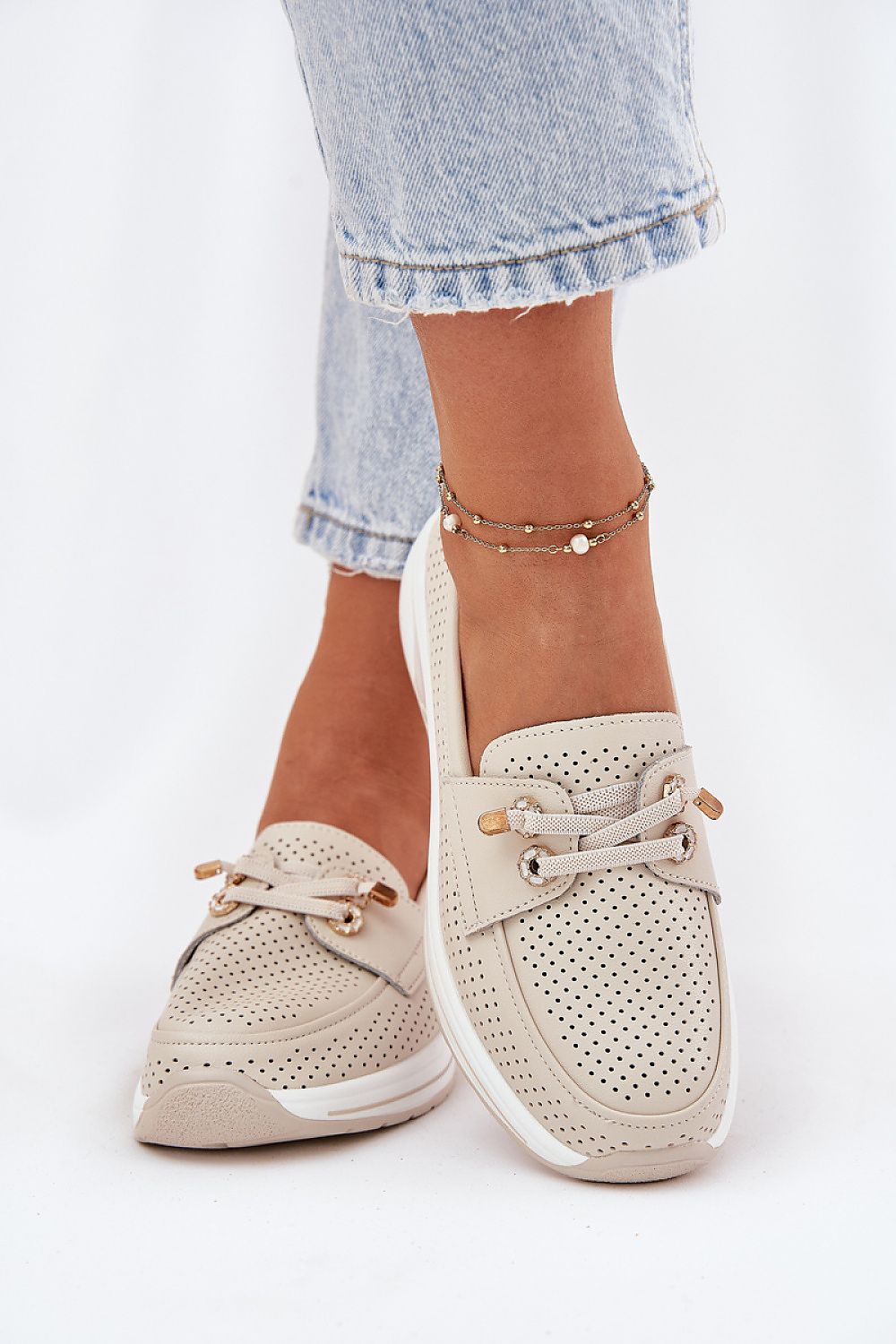 Detalle cercano de los cordones con charms dorados sobre ante perforado brillante.