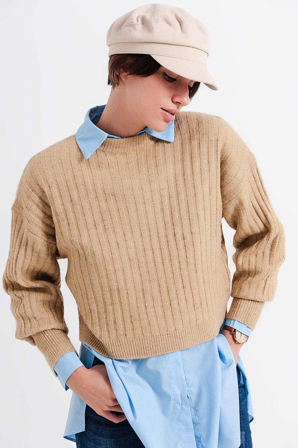 Modelo con jersey cropped de punto de canalé en color beige, llevado sobre una camisa azul.
