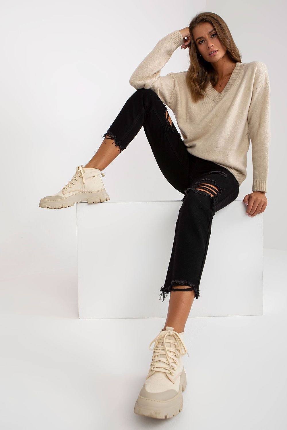 Jersey beige con jeans negros rotos y botas beige en look casual.