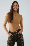 Modelo sonriendo con jersey camel de cuello alto y botones dorados en los puños, combinado con pantalón de leopardo y cinturón negro.