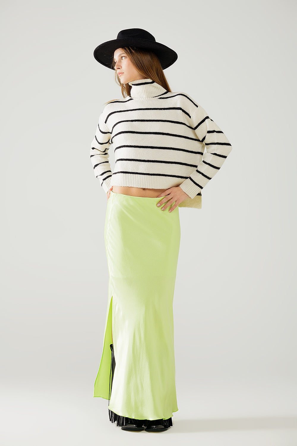 Modelo con jersey cropped de punto a rayas horizontales en crema y negro, con cuello alto y corte amplio.