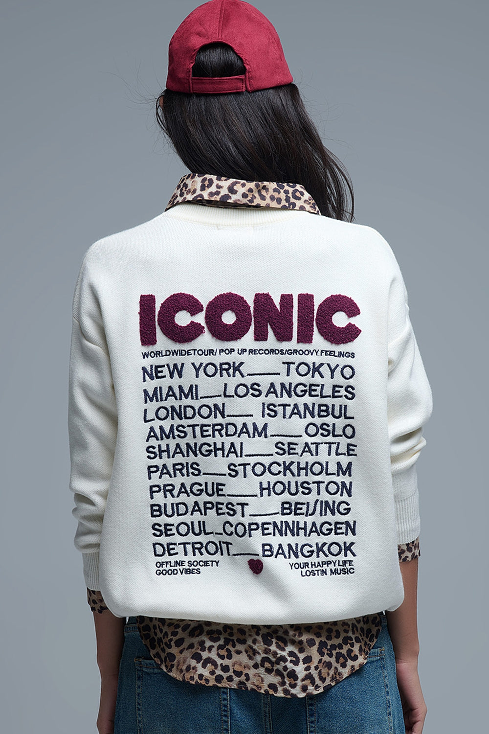 Vista trasera de jersey de punto crema con "ICONIC" en rizo y una lista de ciudades "Global Tour" bordada.