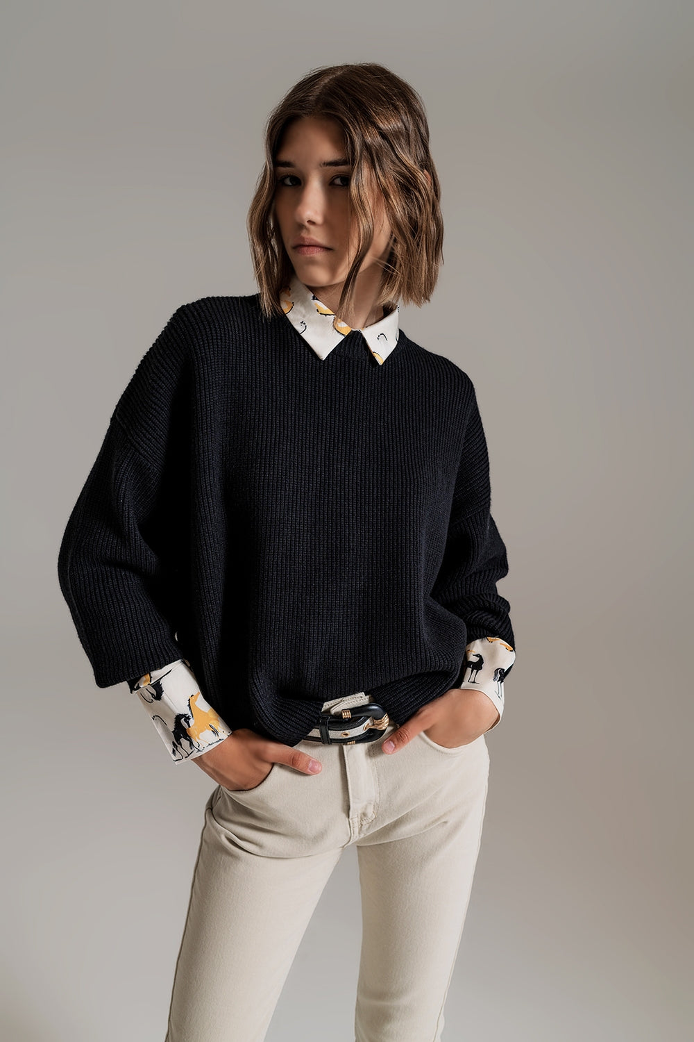Mujer vistiendo jersey negro de punto grueso estilo oversize sobre camisa estampada y pantalones beige.