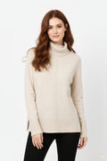 Modelo con jersey oversize de punto suave y cuello vuelto en color beige, combinado con pantalones negros.