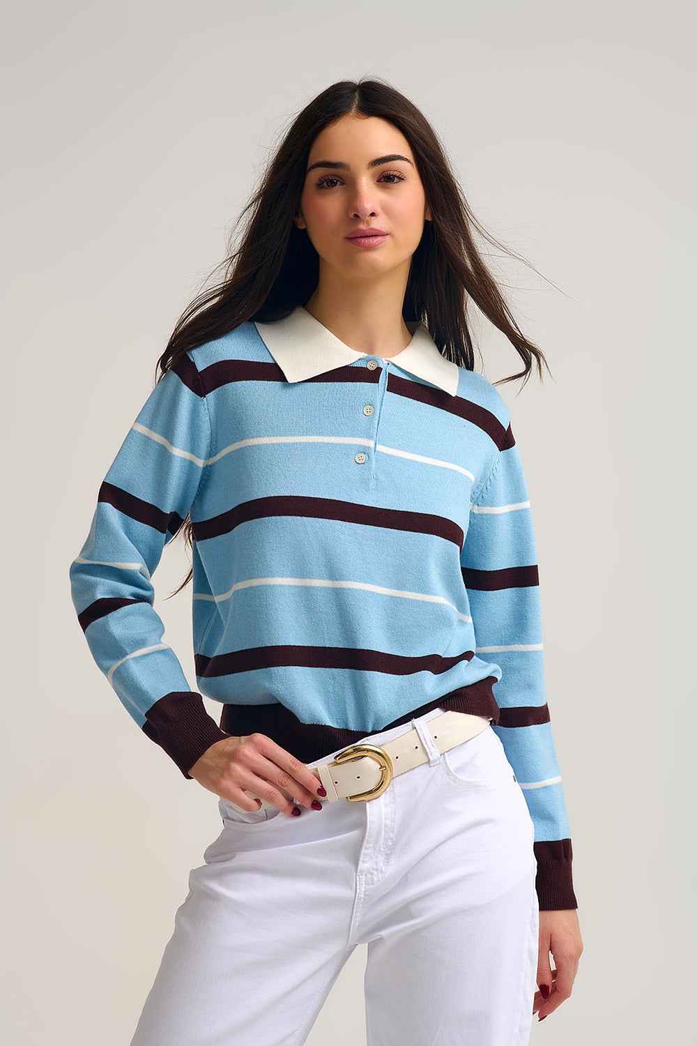 Mujer vistiendo jersey polo azul cielo de rayas con cuello blanco y pantalón blanco con cinturón.