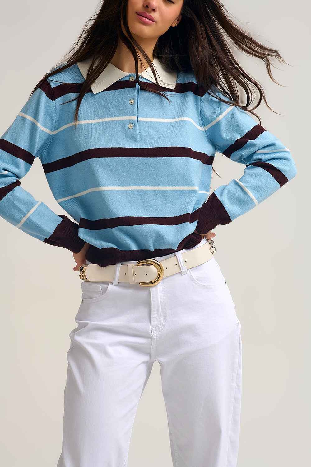 Mujer vistiendo jersey polo azul cielo de rayas con cuello blanco y pantalón blanco con cinturón.