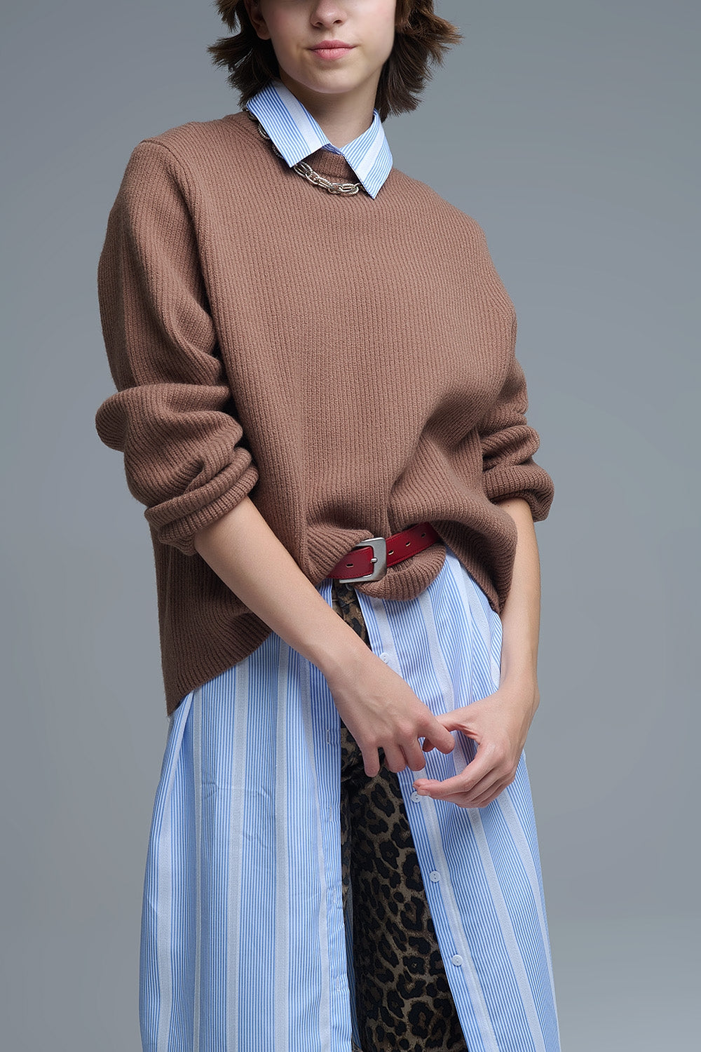 Modelo con jersey de punto acanalado en color camel, de corte amplio y cuello redondo, sobre una camisa de rayas.