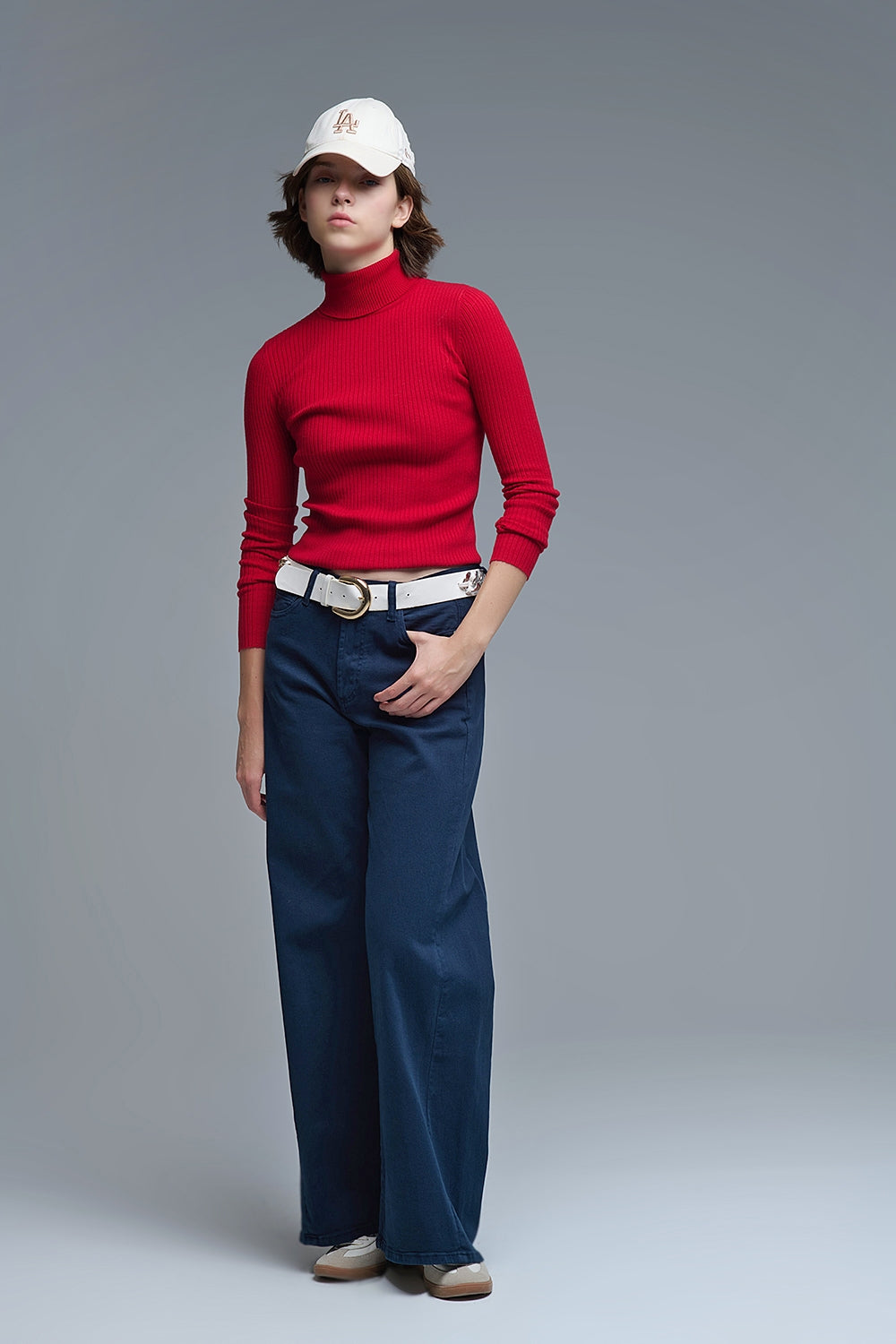 Modelo con jersey de punto de canalé ajustado en color rojo rubí, con cuello alto y manga larga.