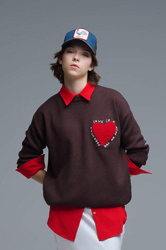 Plano medio de un jersey de punto marrón con un corazón rojo texturizado y el texto 'Love is...' bordado.