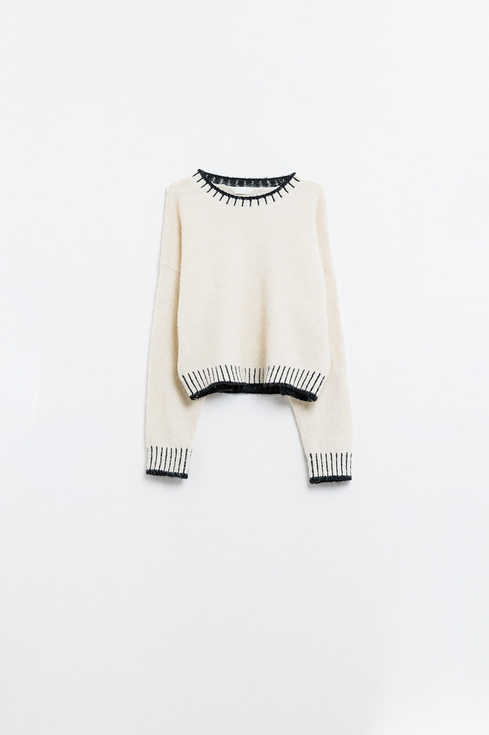 suéter de punto esponjoso color crema con detalles de canalé negro en cuello y puños.