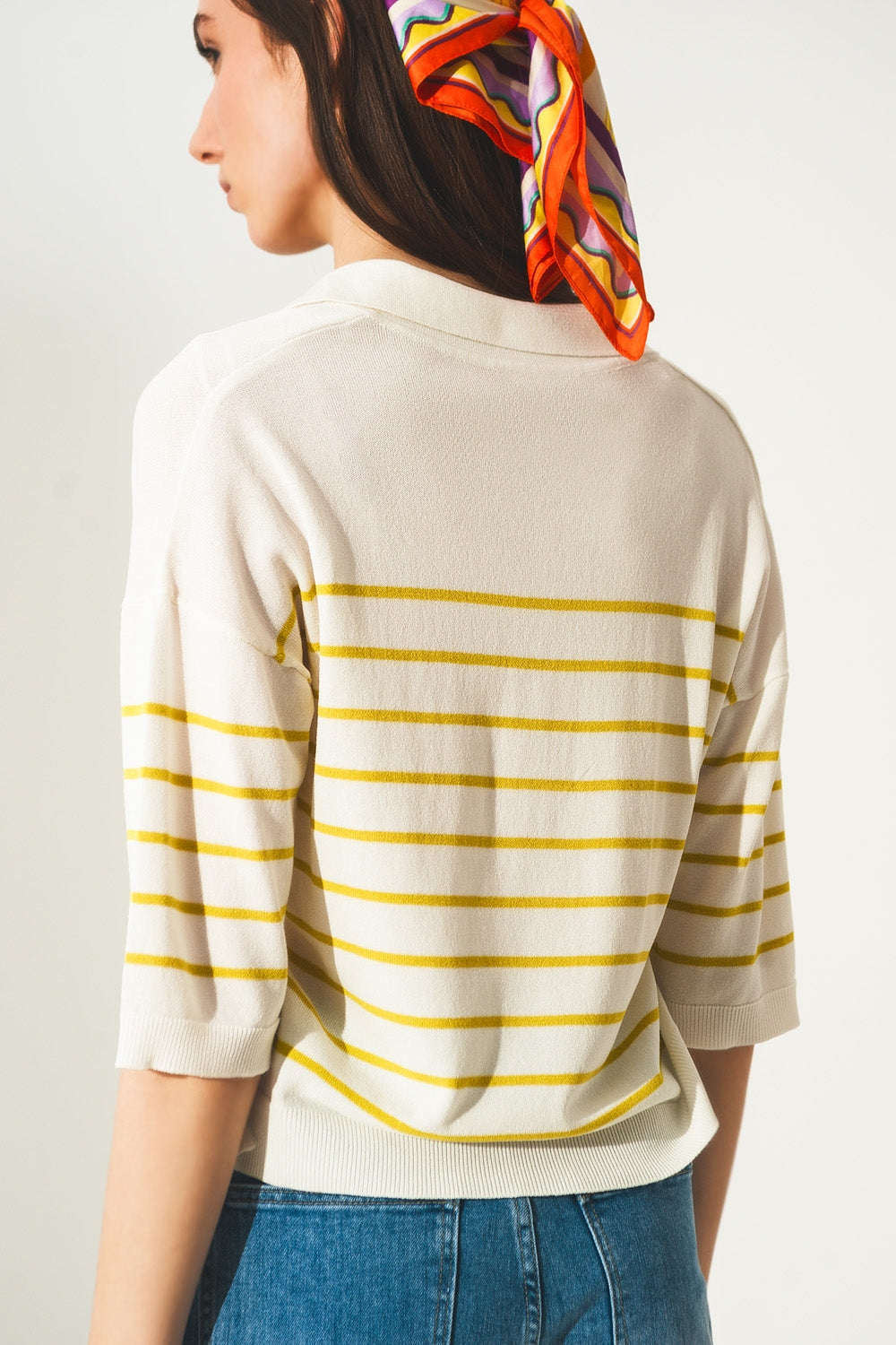 Mujer vistiendo jersey de punto fino con rayas amarillas verdosas, cuello polo y manga tres cuartos, combinado con vaqueros y pañuelo retro.