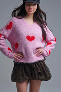 Mujer con boina y jersey rosa oversize de corazones rojos, con falda corta marrón.