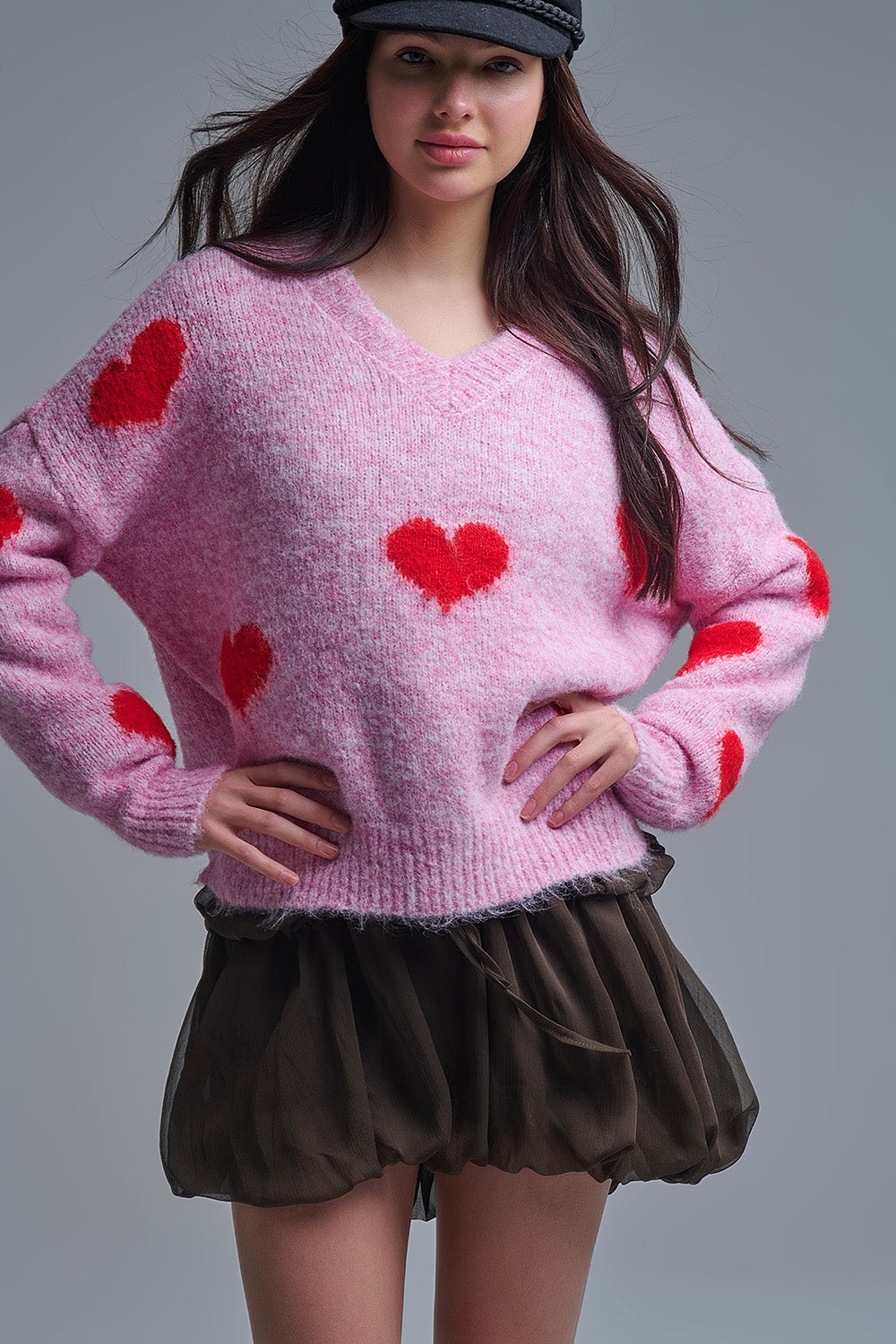 Mujer con boina y jersey rosa oversize de corazones rojos, con falda corta marrón.