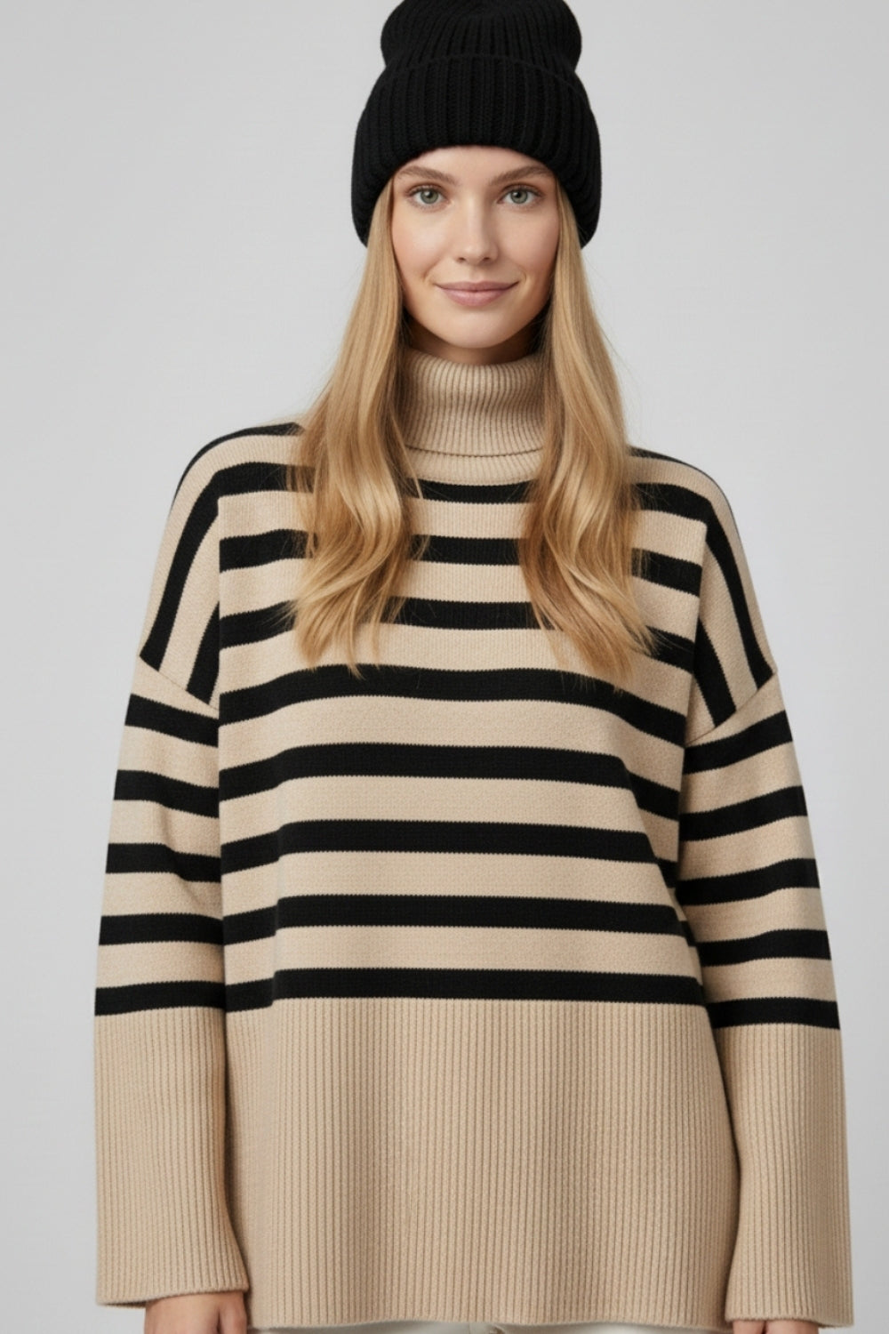 Modelo con jersey oversize de cuello vuelto en color beige con rayas negras horizontales.