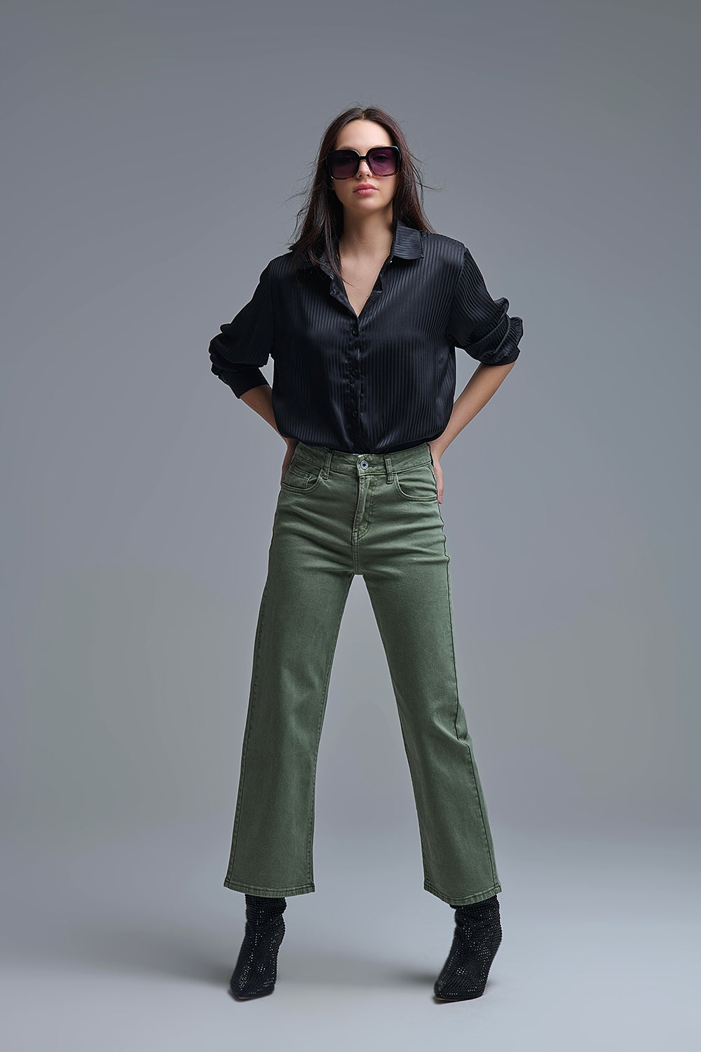 Look completo de mujer con camisa negra de satén a rayas, pantalones verdes y botines negros.