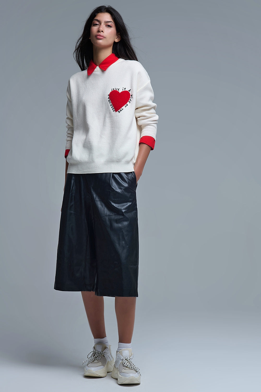 Look completo de mujer con jersey de punto crema con corazón, culottes de piel negros y zapatillas chunky.