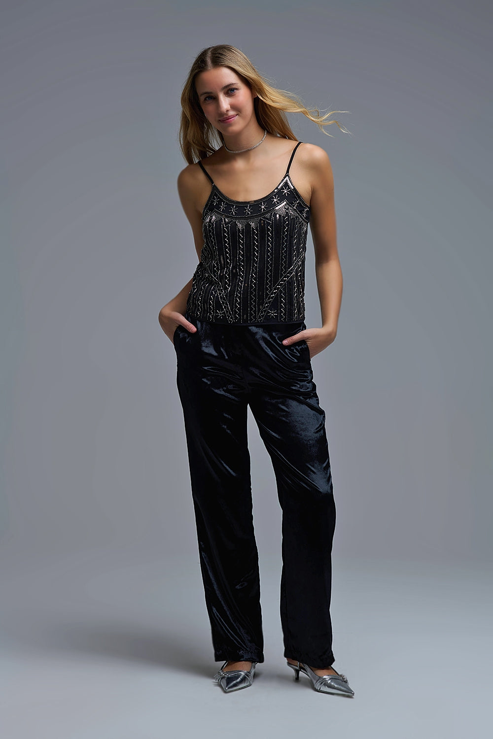 Look de noche elegante con top joya negro bordado y pantalones de vestir oscuros.