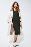 Modelo con look de invierno: vestido midi verde de punto combinado con abrigo largo beige y zapatillas.