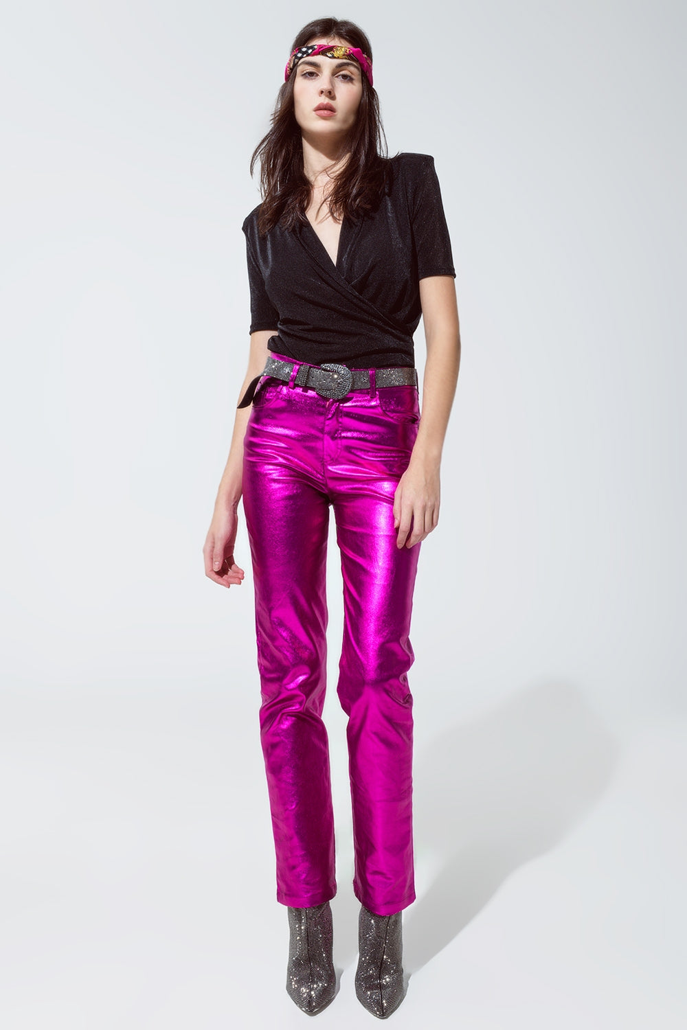 Modelo con look de fiesta de pantalón metalizado fucsia, top negro y botines de glitter.
