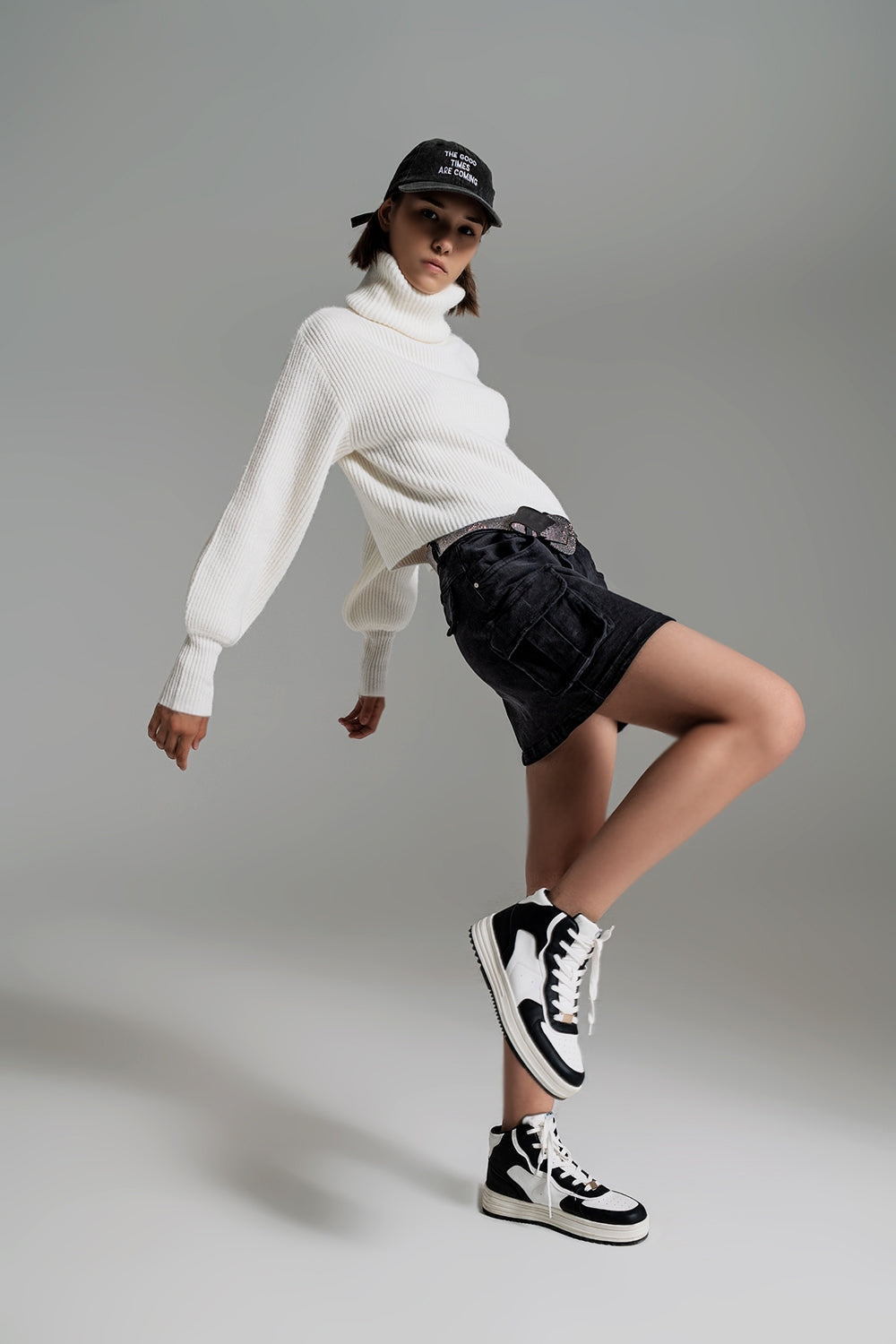 Mujer vistiendo minifalda vaquera negra estilo cargo con bolsillos laterales, cinturón de brillos y zapatillas deportivas.