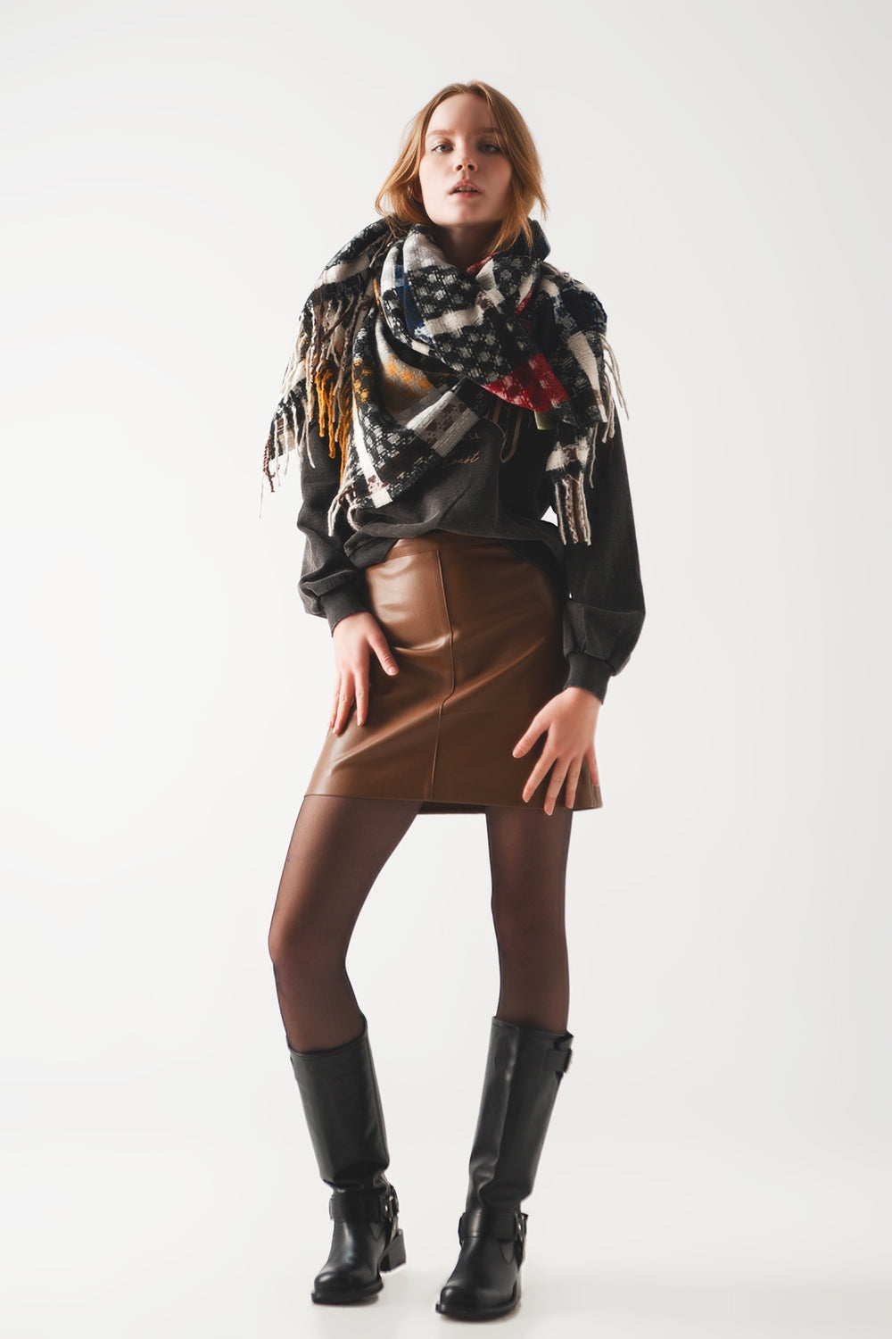 Minifalda de mujer en color camel efecto cuero con costuras vistas, combinada con botas negras y sudadera oscura.