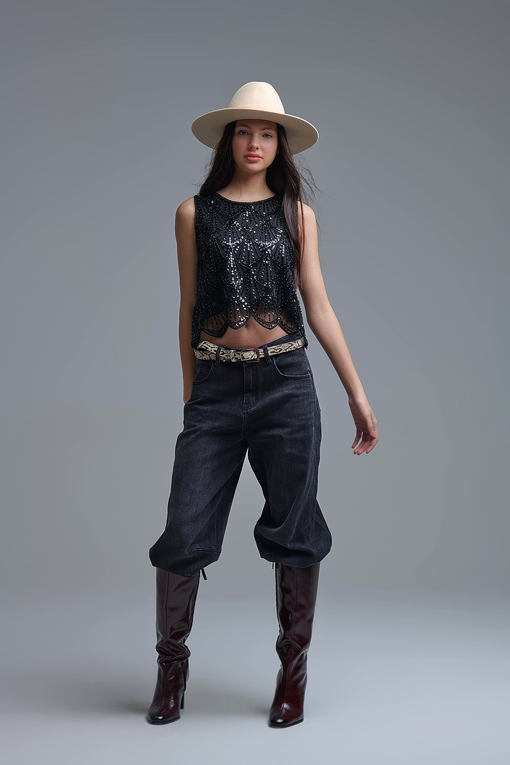 Look de moda con top negro bordado vintage, pantalones anchos y botas altas de charol.