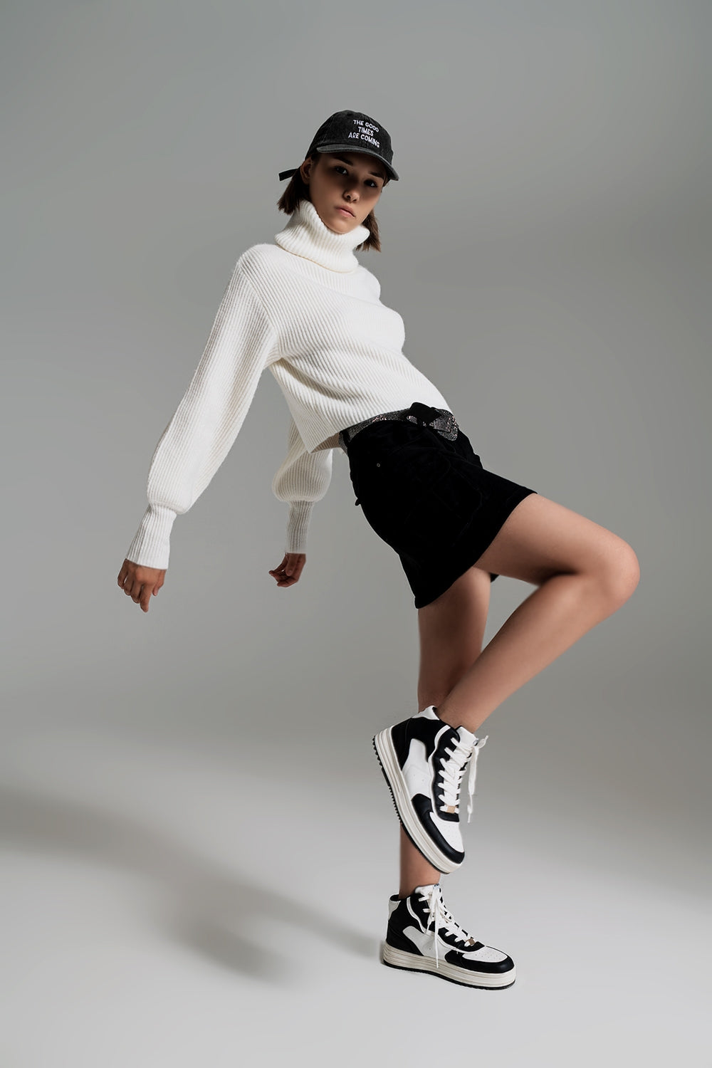 Modelo en movimiento con look juvenil de jersey corto blanco de mangas globo, falda negra y zapatillas altas.