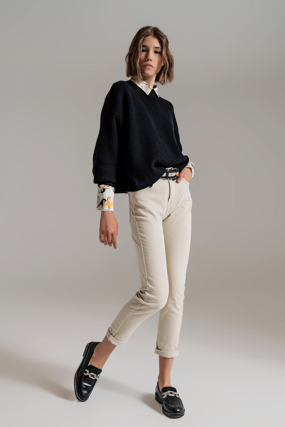 Look completo de mujer con suéter negro holgado, pantalones claros y mocasines negros.