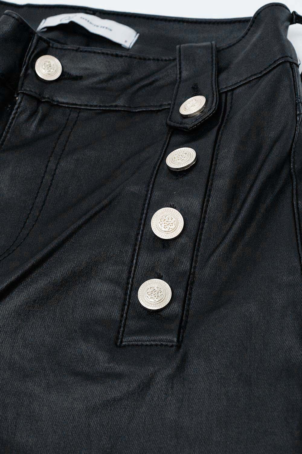 Primer plano de los botones dorados y la cintura de un pantalón de talle alto de efecto piel.