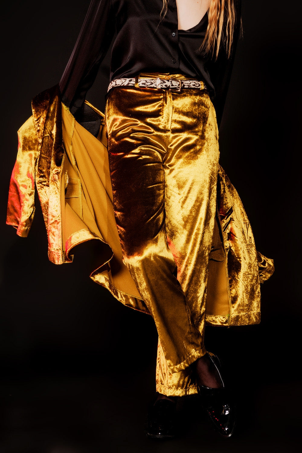 Mujer vistiendo pantalones rectos de terciopelo color oro viejo brillante con camisa negra.