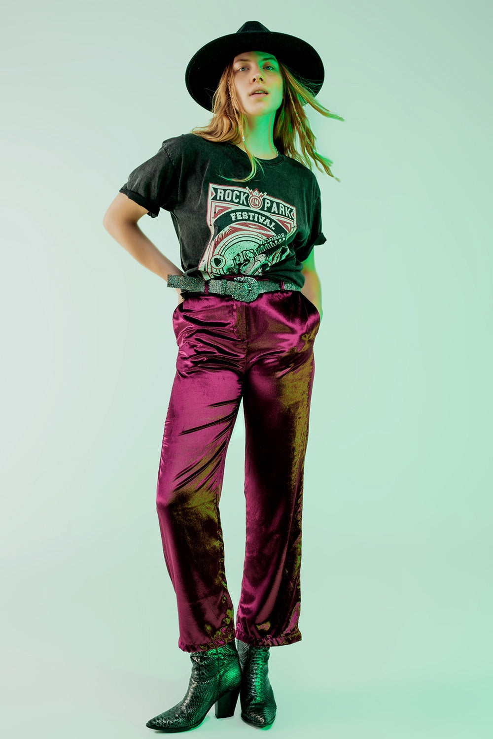 Mujer vistiendo pantalones rectos de terciopelo brillante color magenta combinados con camiseta rockera y botines.