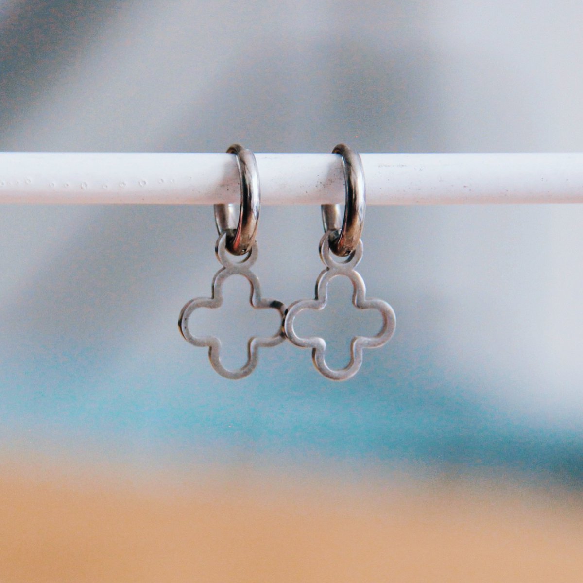 Par de pendientes de aro pequeños en acero inoxidable plateado con colgante de trébol abierto de la suerte.