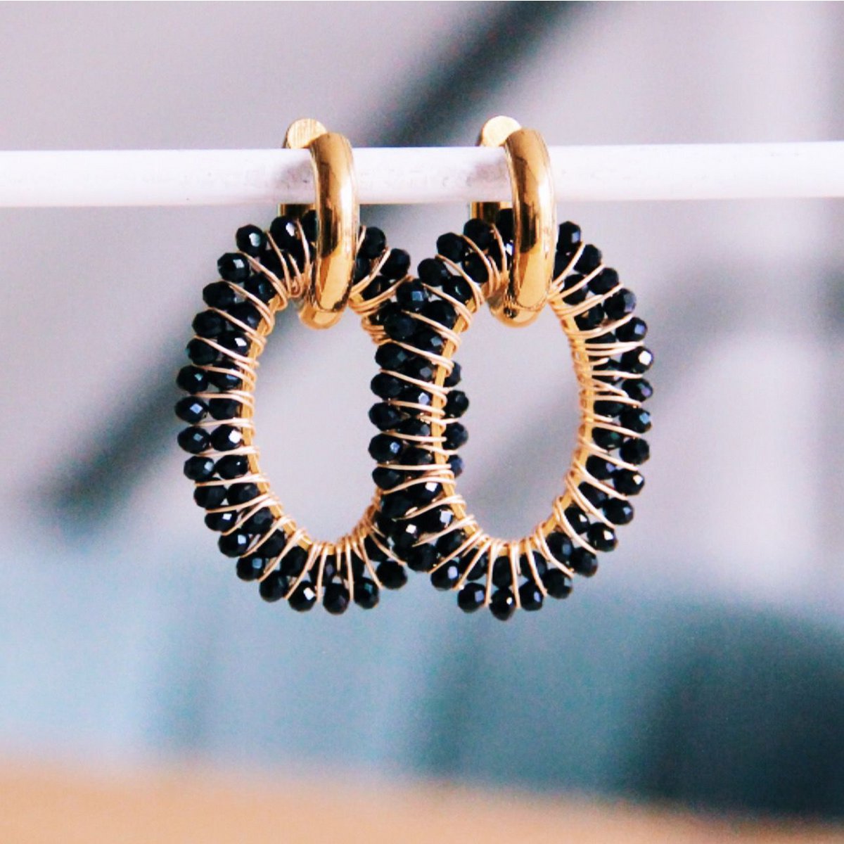 Par de pendientes de aro dorados con colgante ovalado grande tejido a mano con cuentas negras facetadas.