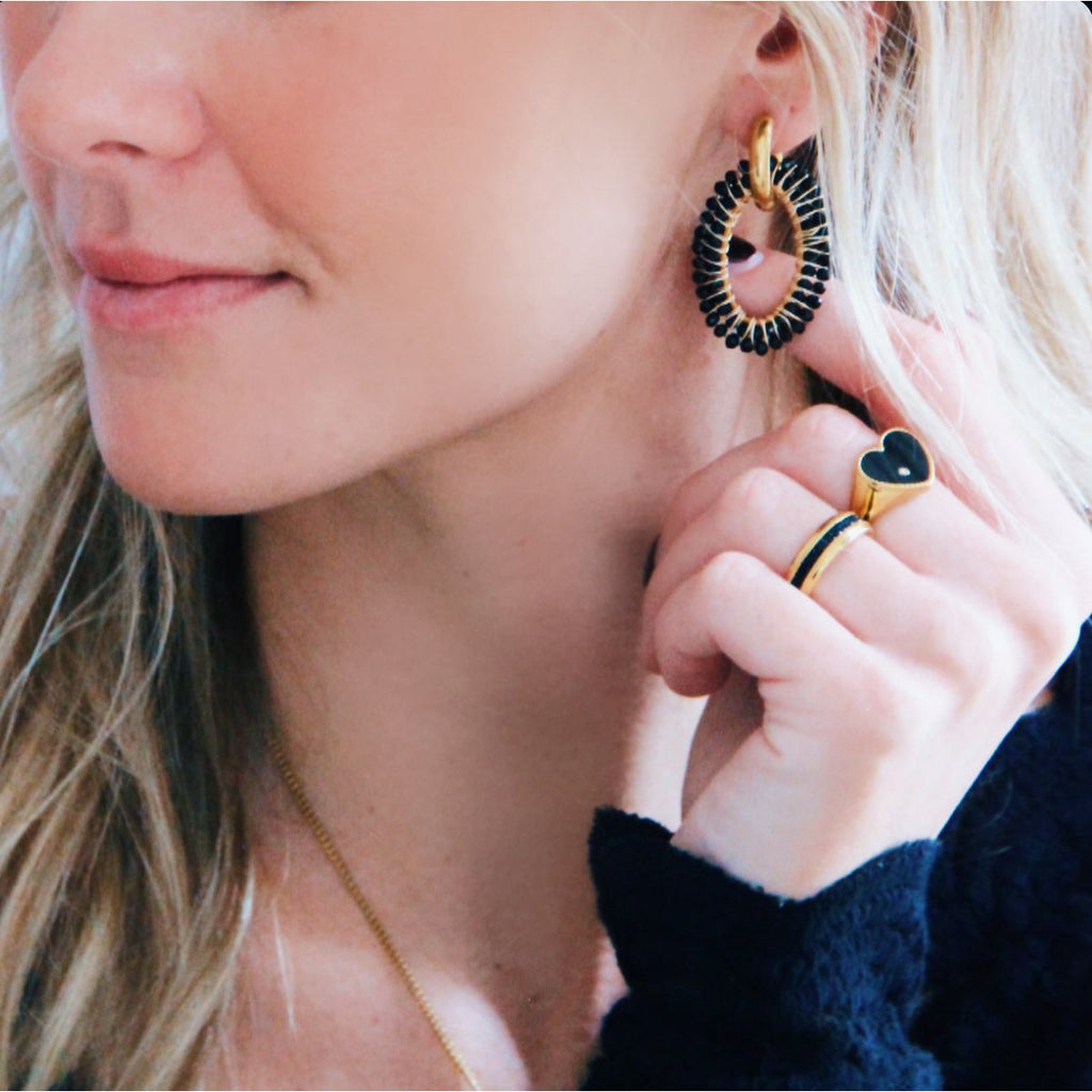 Primer plano mujer llevando pendientes ovalados tejidos con cuentas negras y anillos a juego.