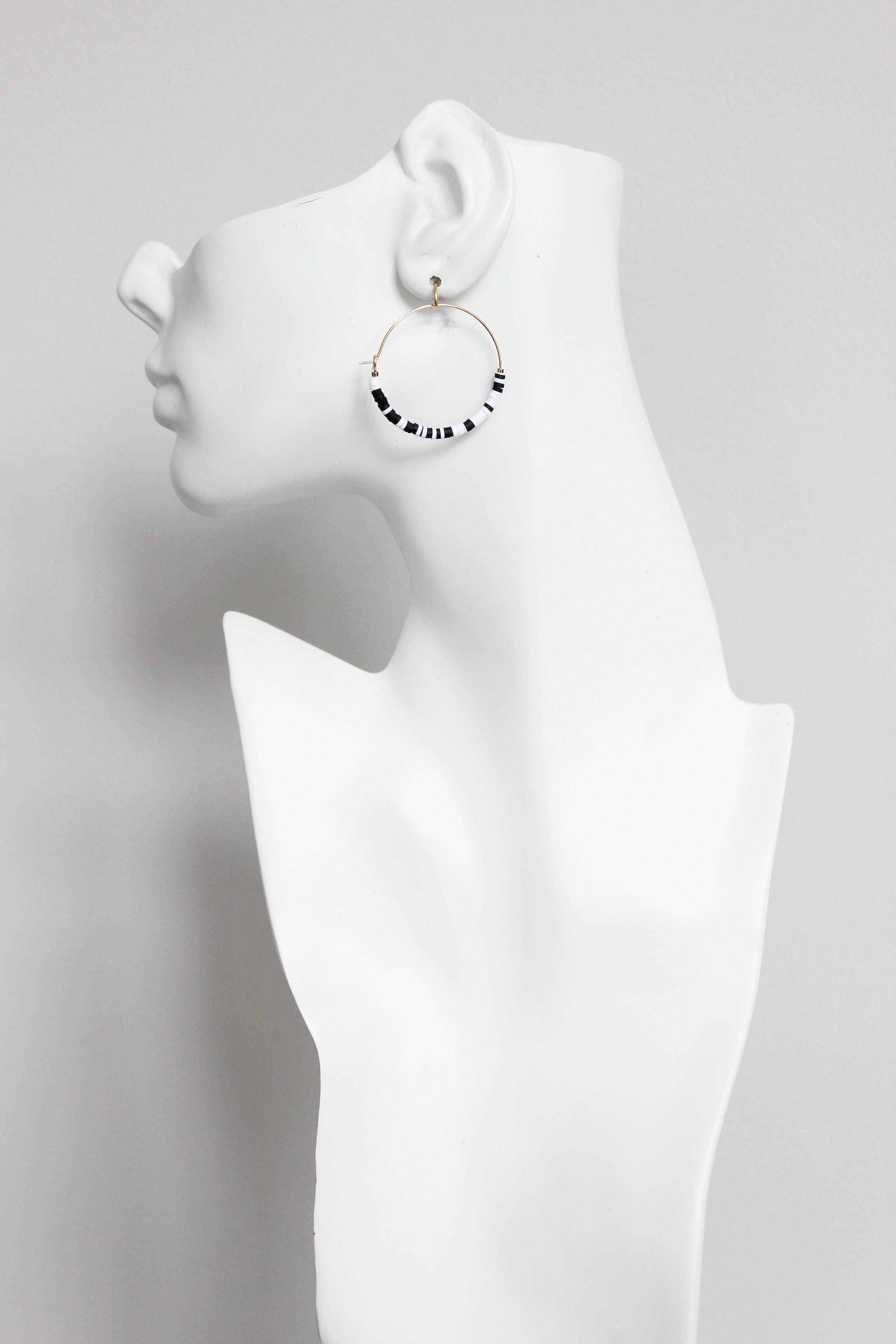 Pendientes de aro blancos y negros vistos en maniquí blanco. Diseño dorado elegante de David Aubrey en estilo Art Decó.