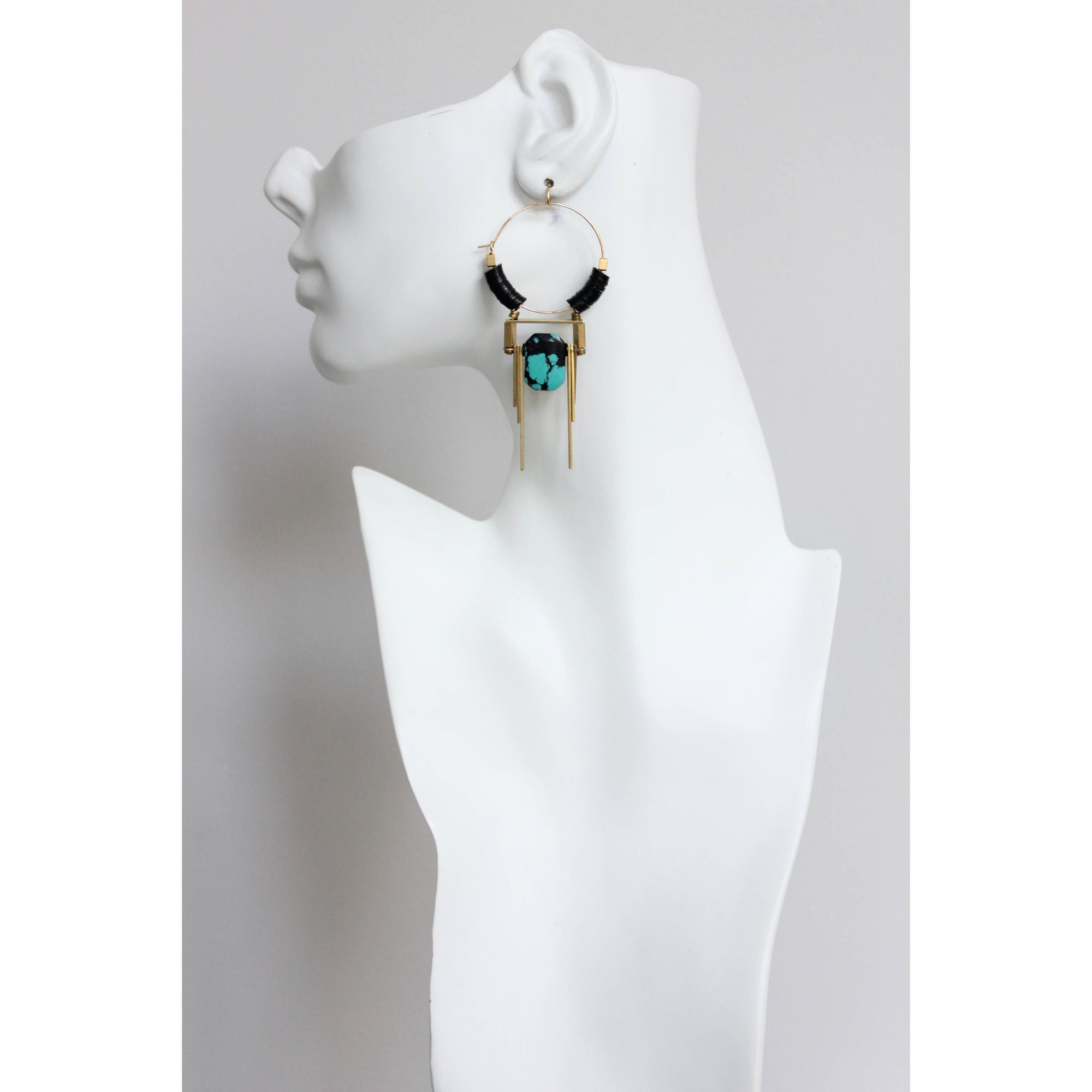 Pendientes colgantes de David Aubrey con turquesa y detalles en latón vistos sobre maniquí blanco, estilo moderno y estructurado.