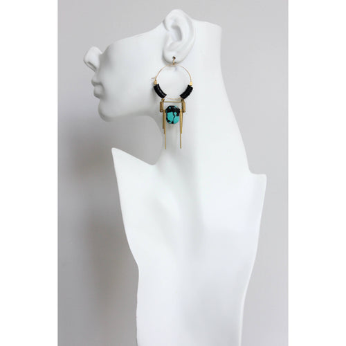 Pendientes colgantes de David Aubrey con turquesa y detalles en latón vistos sobre maniquí blanco, estilo moderno y estructurado.