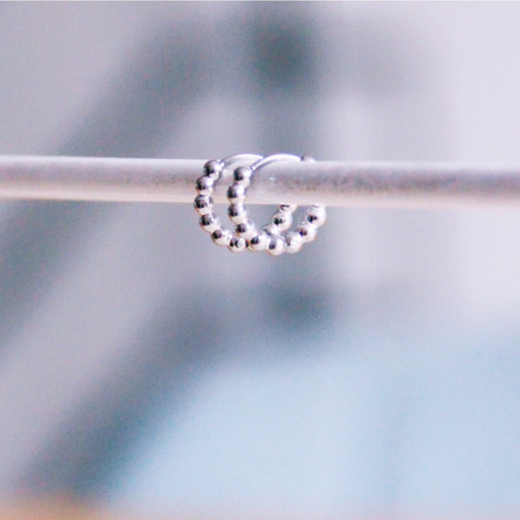 Detalle de aros pequeños plateados con textura de esferas colgados en expositor.