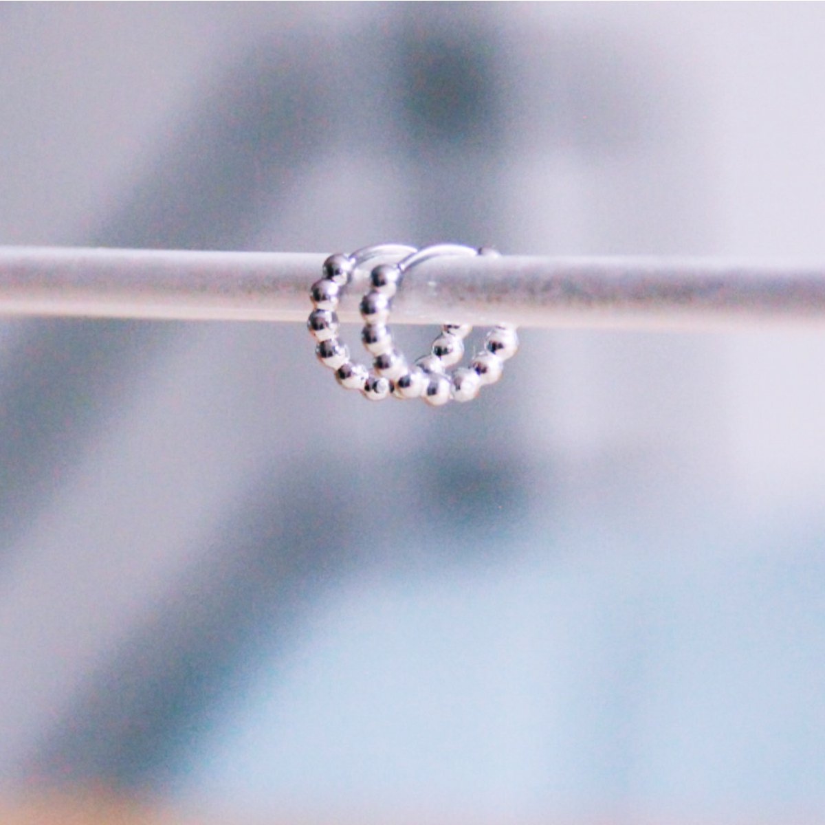 Detalle de aros pequeños plateados con textura de esferas colgados en expositor.