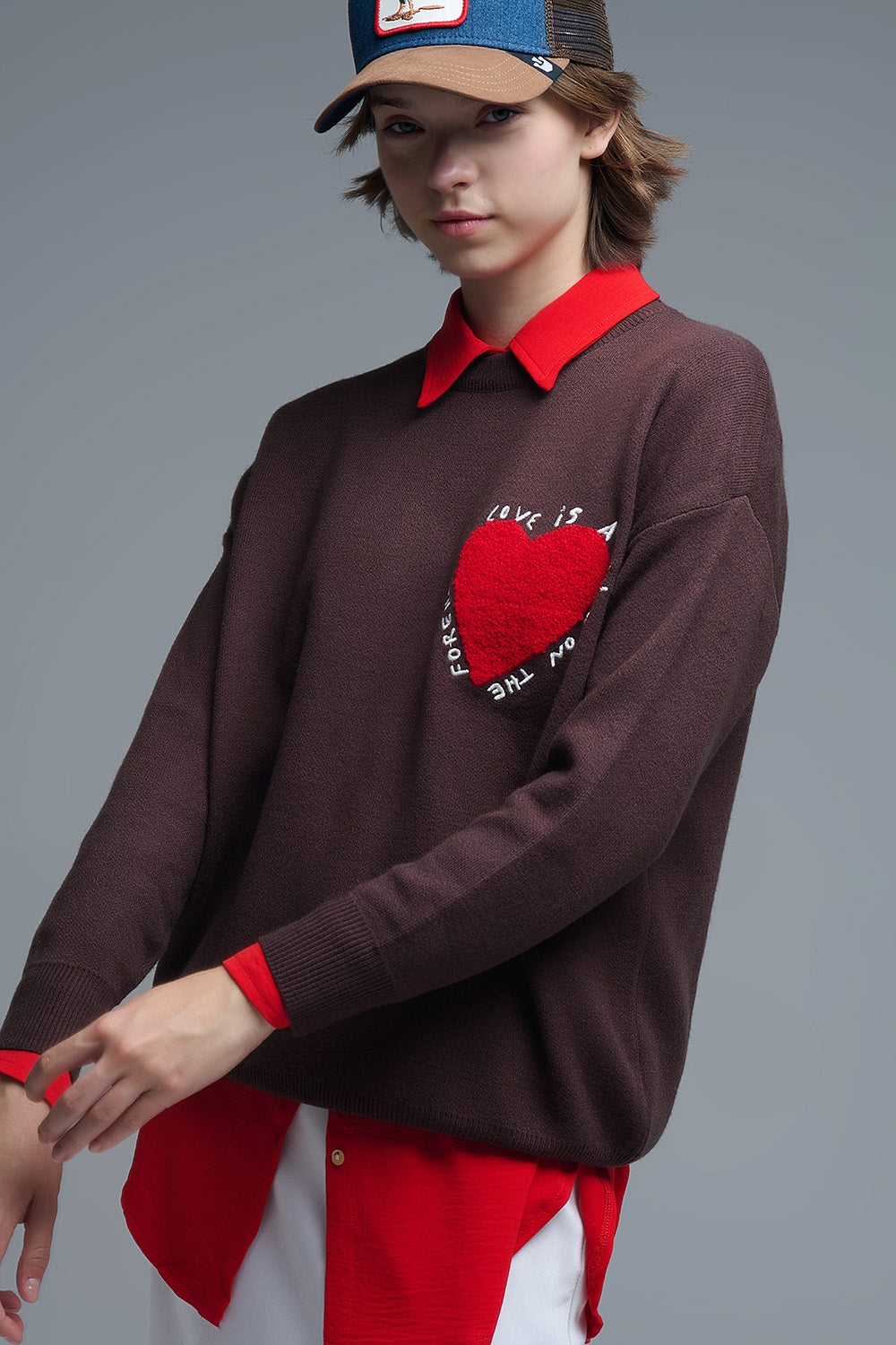 Vista de perfil de una modelo con jersey oversize marrón de hombros caídos y bordado de corazón.