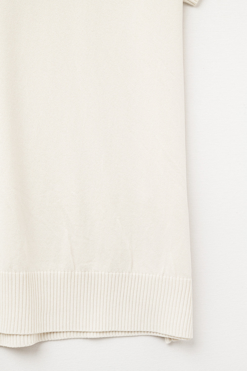 Polo de punto fino para mujer en color crema, con cuello en V sin botones y corte relajado. Detalle tejido.