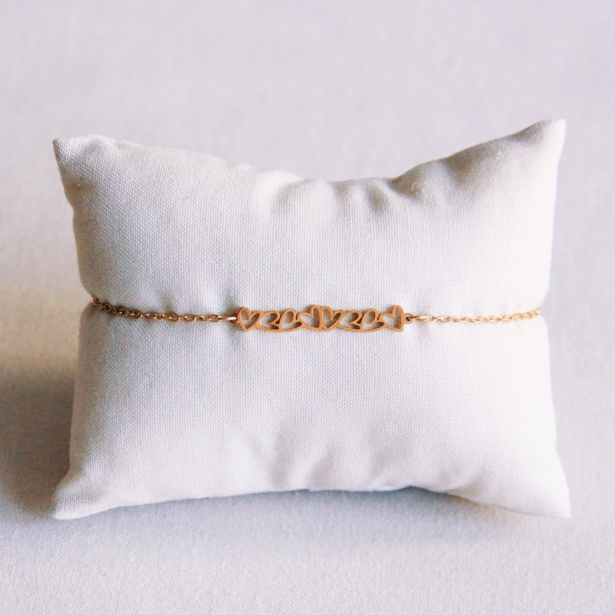 Pulsera minimalista dorada de acero inoxidable con detalle central de corazones entrelazados