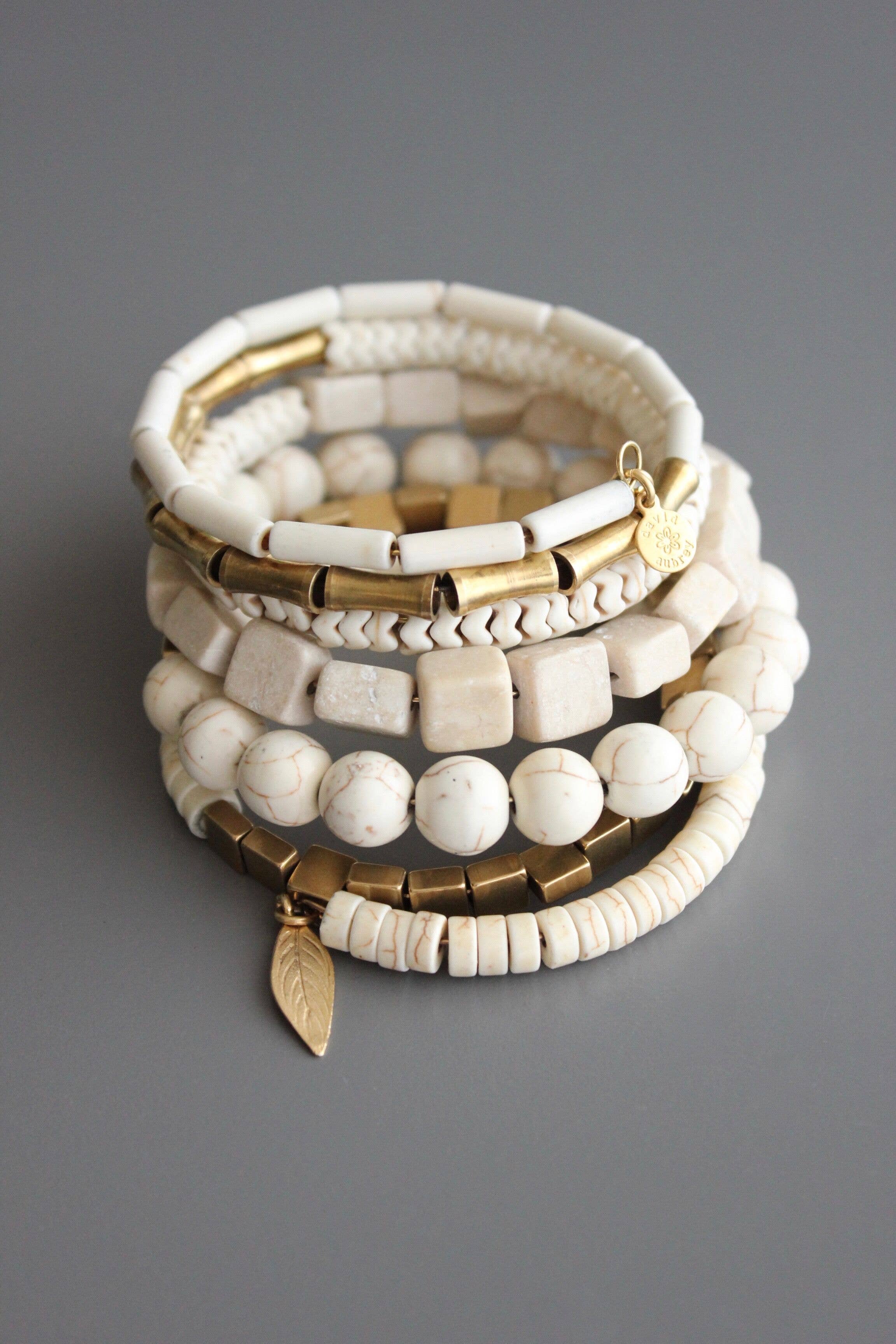 Pulsera envolvente de magnesita natural en tonos crema con detalles de latón dorado y colgante de hoja. Diseño artesanal exclusivo de David Aubrey