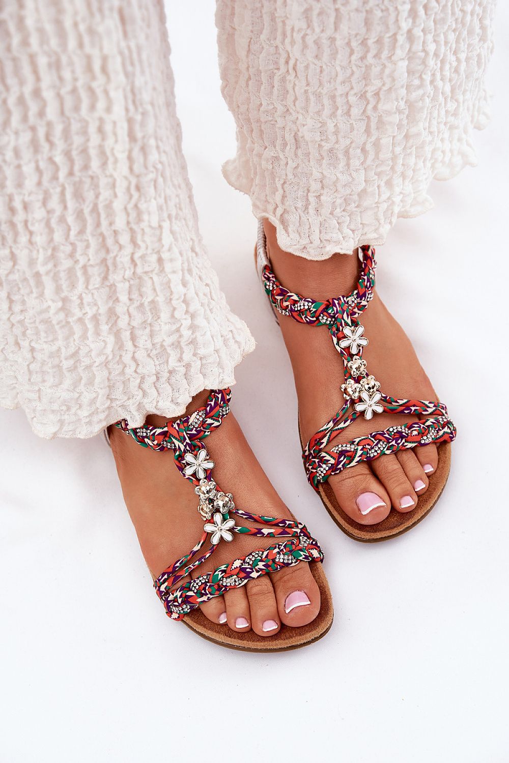 Mujer luciendo sandalias boho multicolor con pantalón blanco