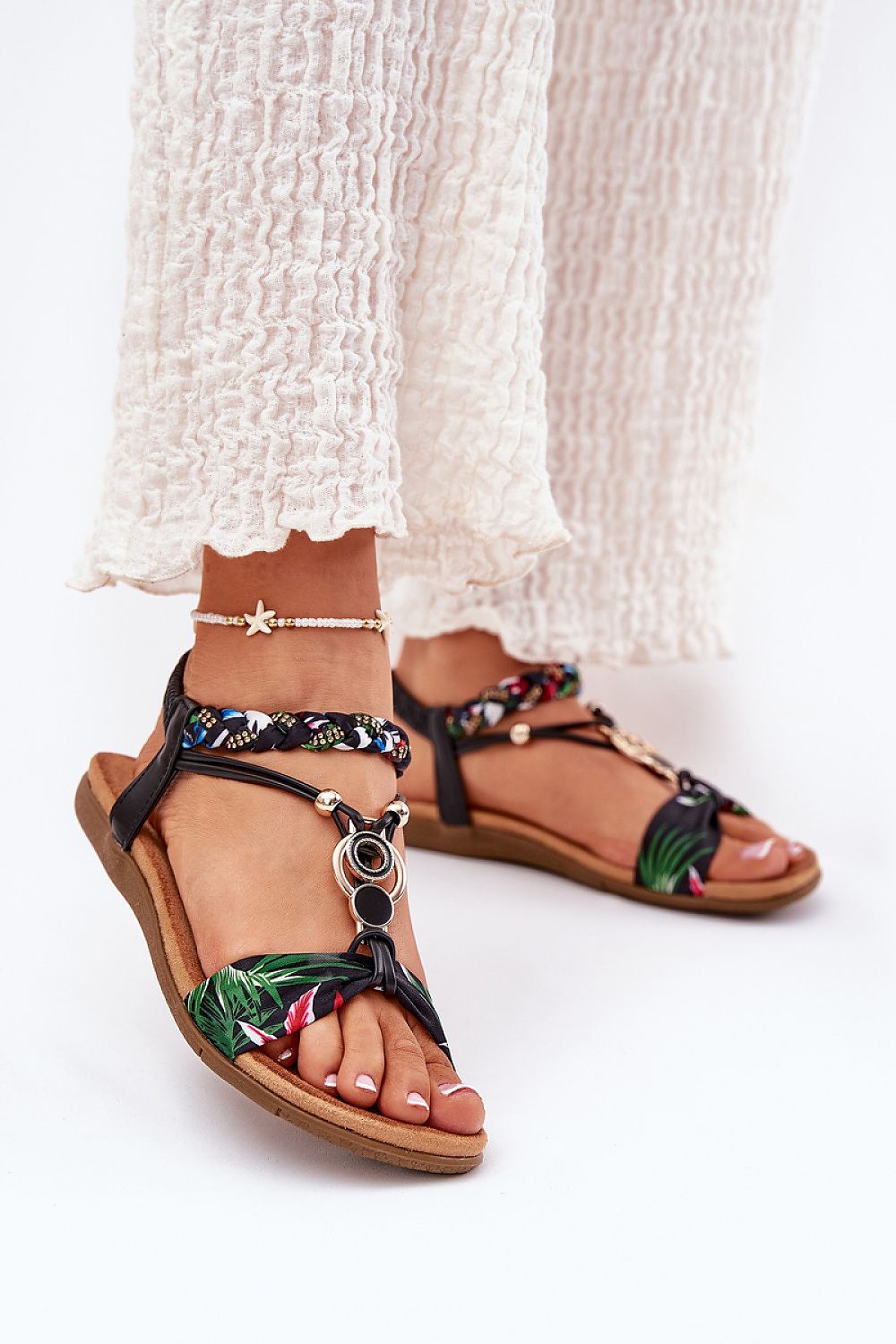 Mujer con pantalón blanco tipo palazzo usando sandalias tropicales con tiras trenzadas.