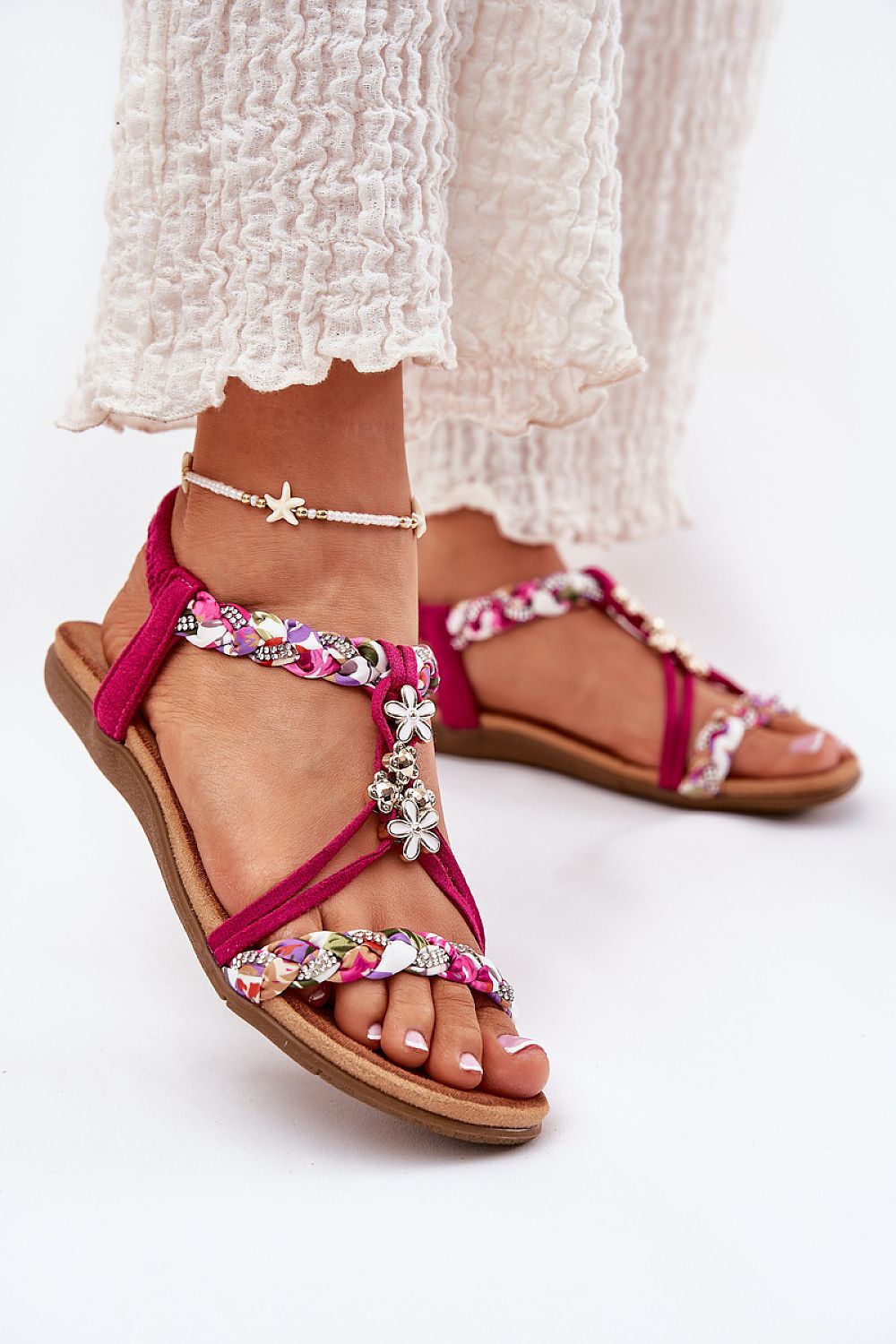 Mujer con sandalias fucsia trenzadas y decoración floral brillante.